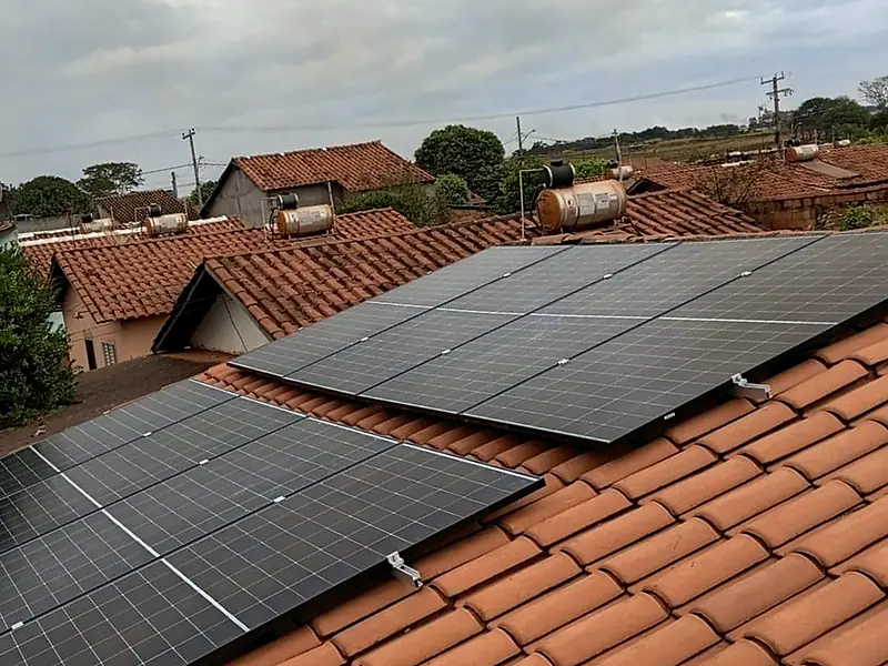 Painéis solares instalados em telhado cerâmico, com casas e o céu ao fundo